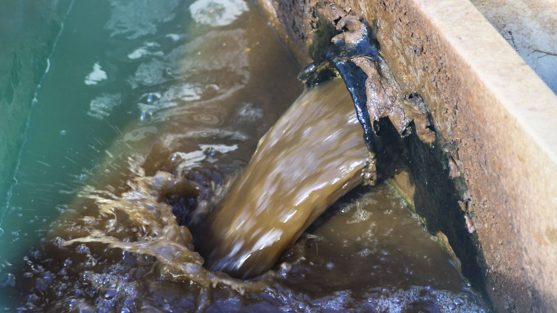 Industrial wastewater discharge flowing from pipe into treatment basin at California facility