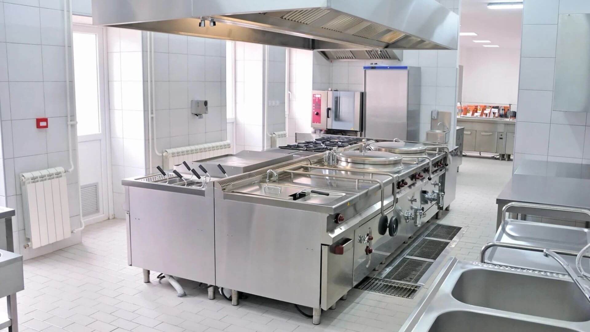 Modern commercial kitchen with stainless steel cooking equipment and floor drain system to support FOG compliance in California food service facility